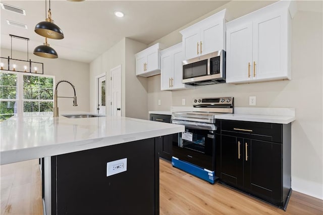 kitchen with a center island with sink, stainless steel appliances, light wood-type flooring, hanging light fixtures, and sink