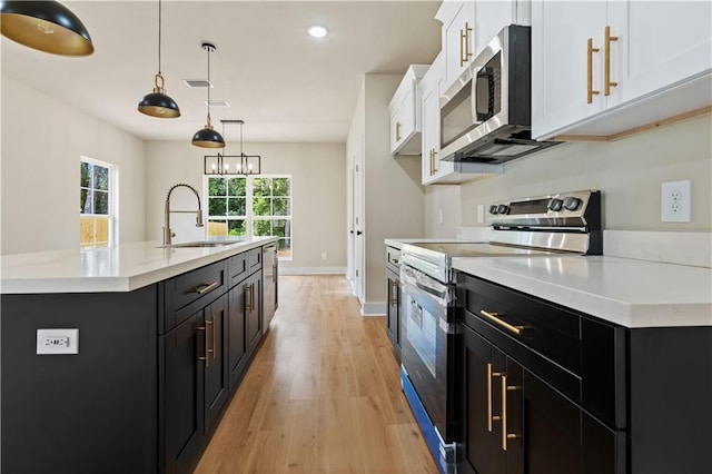 kitchen with a center island with sink, stainless steel appliances, hanging light fixtures, sink, and white cabinetry