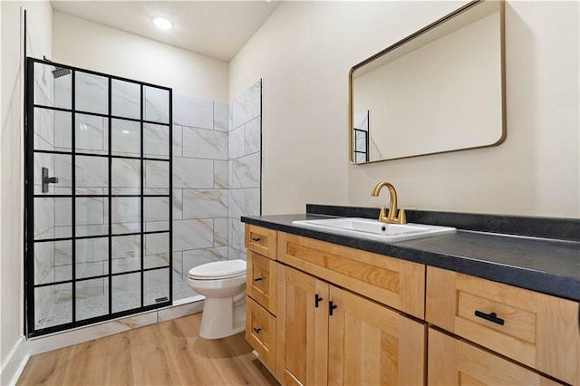 bathroom featuring toilet, wood-type flooring, vanity, and tiled shower