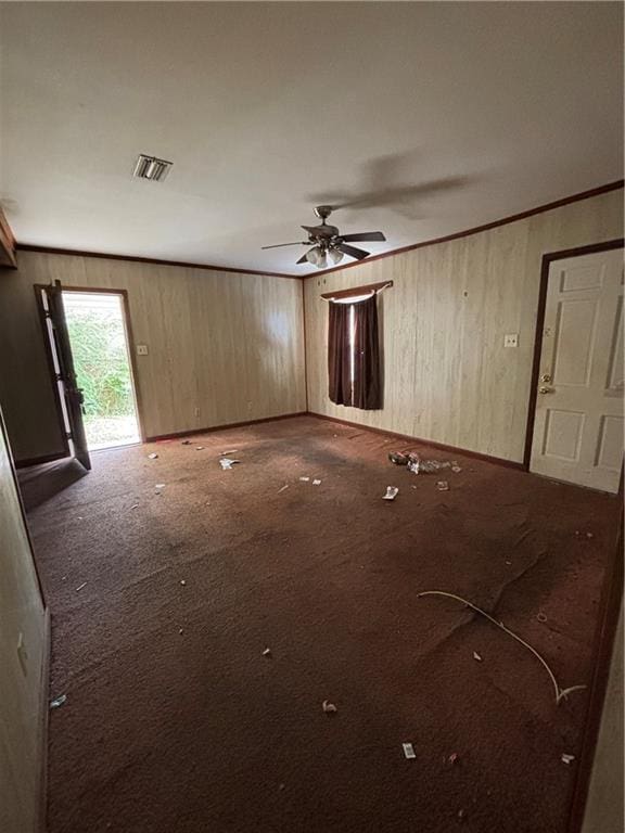 carpeted empty room with crown molding, ceiling fan, and wood walls