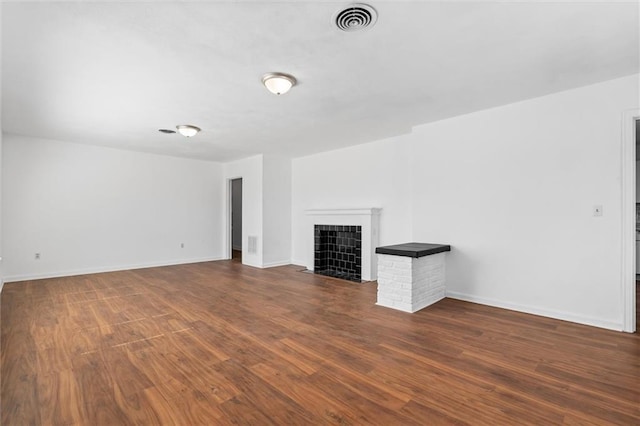 unfurnished living room with baseboards, visible vents, dark wood-type flooring, and a tiled fireplace