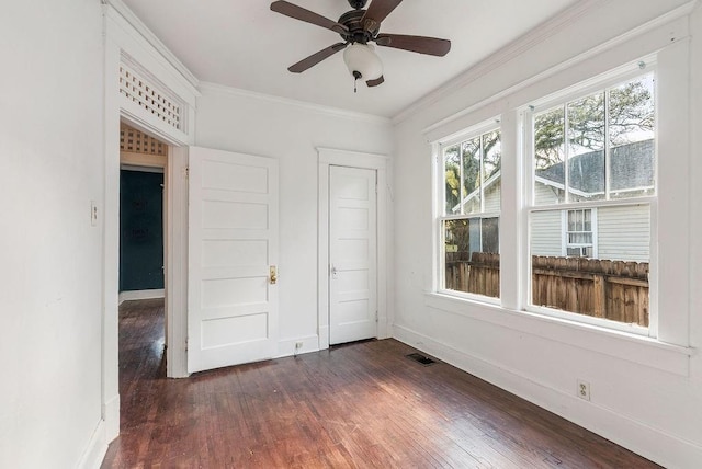 empty room with baseboards, dark wood-style flooring, ornamental molding, and visible vents