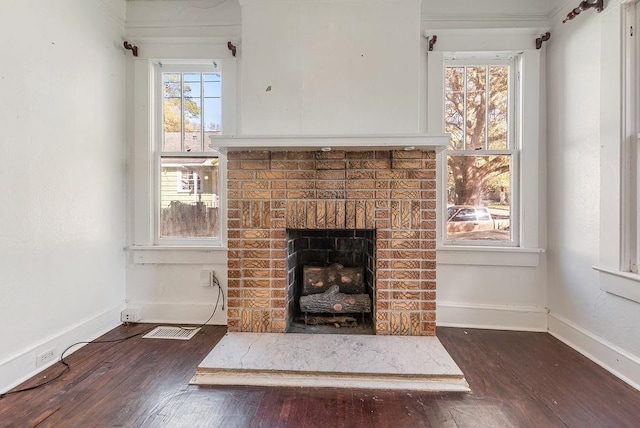 unfurnished living room featuring wood-type flooring, a brick fireplace, baseboards, and visible vents