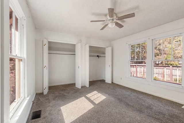 unfurnished bedroom featuring multiple windows, visible vents, two closets, and carpet floors