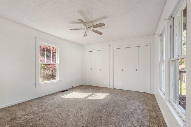 unfurnished bedroom featuring two closets, carpet, baseboards, a textured ceiling, and ceiling fan