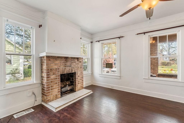 unfurnished living room with dark wood-type flooring, visible vents, a healthy amount of sunlight, and a brick fireplace