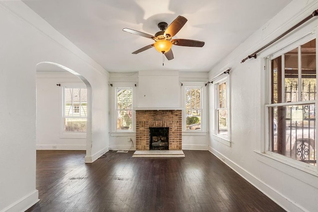 unfurnished living room with hardwood / wood-style flooring, baseboards, a fireplace, ceiling fan, and arched walkways