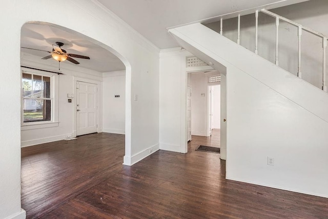 interior space with baseboards, ceiling fan, wood finished floors, ornamental molding, and arched walkways