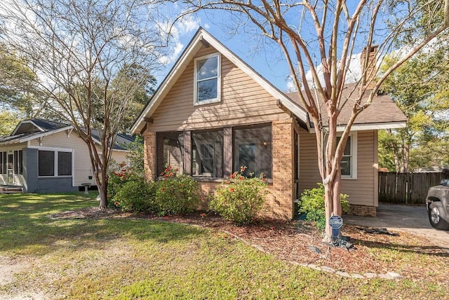 bungalow with a sunroom, brick siding, a front yard, and fence