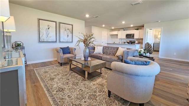 living area with baseboards, visible vents, wood finished floors, and recessed lighting