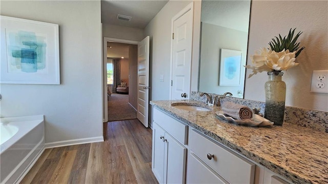 bathroom featuring a garden tub, wood finished floors, vanity, visible vents, and baseboards