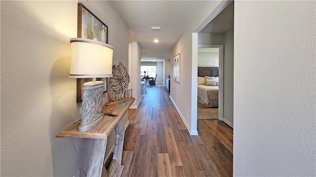 corridor with dark wood-type flooring, a textured wall, and baseboards