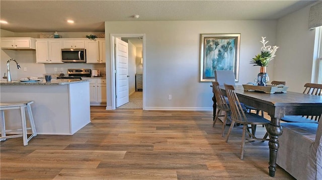 kitchen featuring light stone counters, light wood-style flooring, stainless steel appliances, white cabinetry, and baseboards