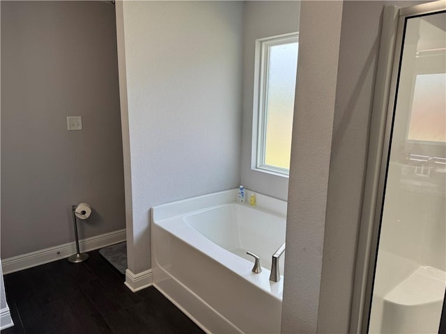 bathroom featuring a stall shower, a garden tub, baseboards, and wood finished floors