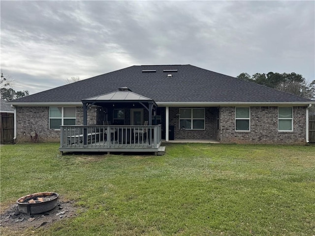 rear view of property with a deck, an outdoor fire pit, brick siding, a gazebo, and a yard