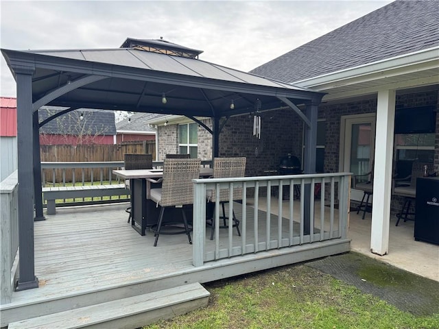 wooden terrace featuring fence, outdoor dining area, and a gazebo