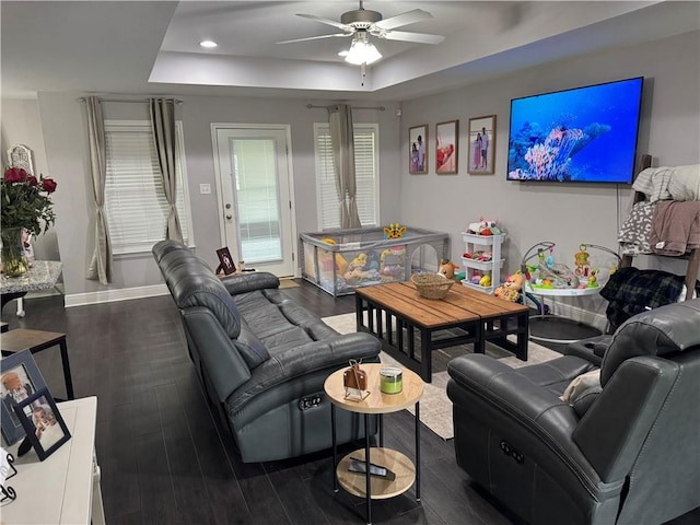 living area featuring recessed lighting, dark wood-type flooring, a ceiling fan, baseboards, and a raised ceiling