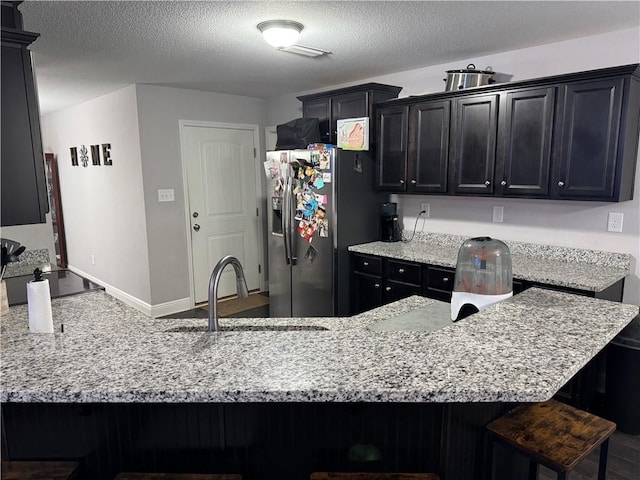 kitchen featuring stainless steel refrigerator with ice dispenser, a sink, dark cabinets, a peninsula, and a kitchen breakfast bar