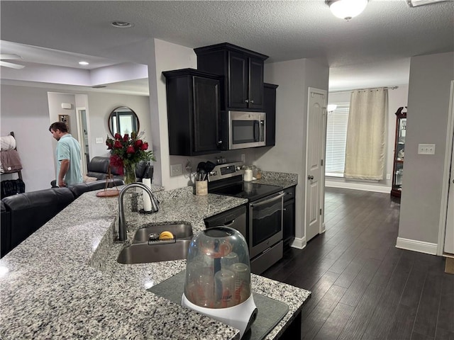 kitchen with stainless steel appliances, open floor plan, a sink, light stone countertops, and dark cabinetry