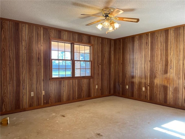 unfurnished room with a textured ceiling, wooden walls, a ceiling fan, and baseboards