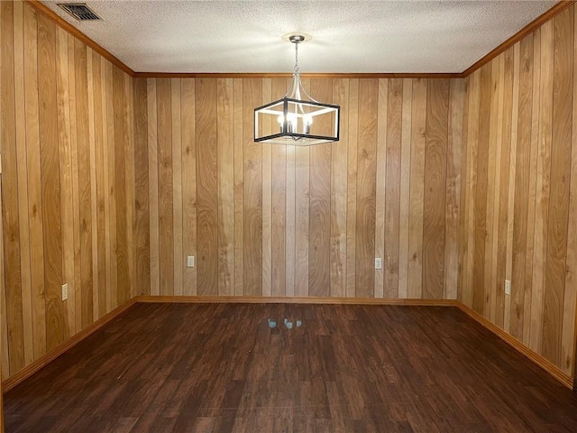 unfurnished dining area featuring wood walls, dark hardwood / wood-style floors, a textured ceiling, and a notable chandelier