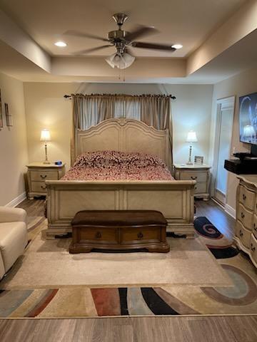 bedroom featuring ceiling fan, light hardwood / wood-style floors, and a tray ceiling