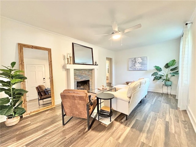 living room with wood-type flooring, a stone fireplace, and ceiling fan