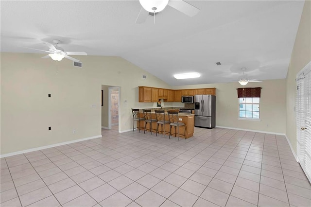 kitchen with kitchen peninsula, lofted ceiling, a kitchen breakfast bar, light tile patterned flooring, and stainless steel appliances