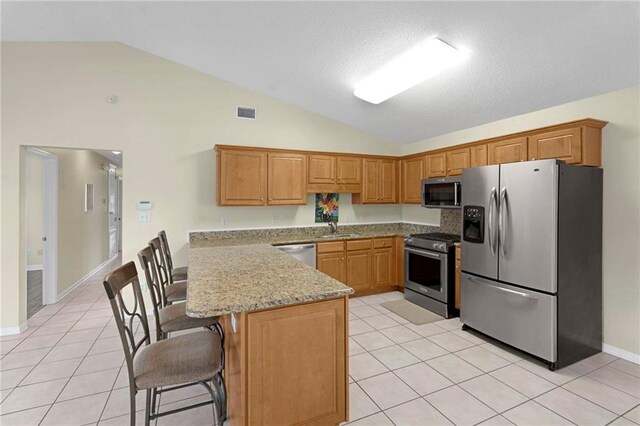 kitchen featuring appliances with stainless steel finishes, light tile patterned flooring, a kitchen bar, vaulted ceiling, and light stone counters