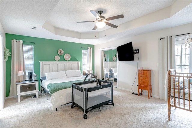 bedroom with light carpet, ceiling fan, a raised ceiling, and a textured ceiling