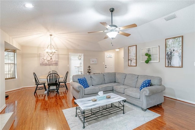 living room with ceiling fan with notable chandelier, wood-type flooring, vaulted ceiling, and a textured ceiling