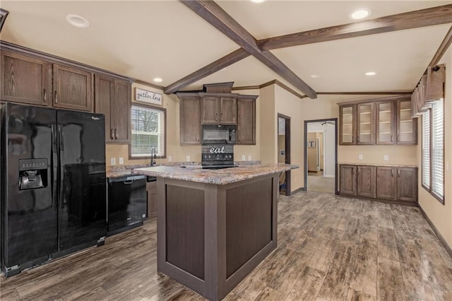 kitchen featuring black appliances, vaulted ceiling with beams, hardwood / wood-style floors, light stone countertops, and a kitchen island