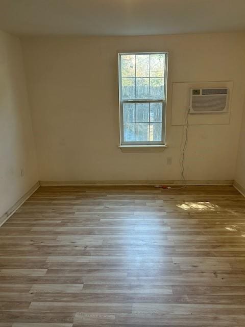 unfurnished room with an AC wall unit, baseboards, and wood finished floors
