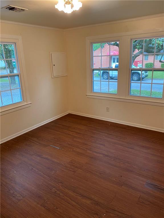 spare room featuring baseboards, visible vents, dark wood-style flooring, an inviting chandelier, and crown molding