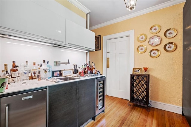 bar featuring sink, fridge, ornamental molding, and light wood-type flooring