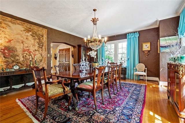 dining area featuring light hardwood / wood-style flooring, a notable chandelier, a textured ceiling, and ornamental molding