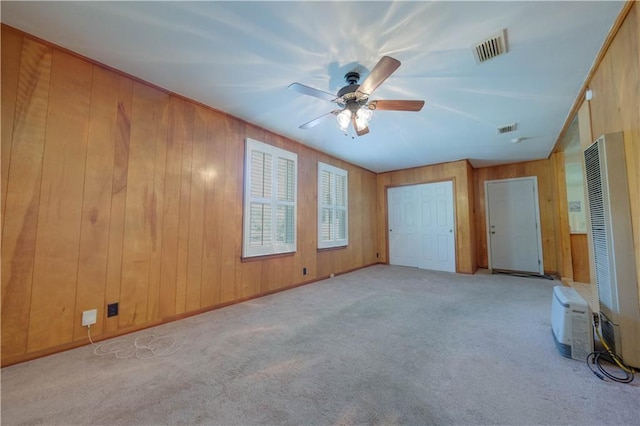 unfurnished living room with wooden walls, ceiling fan, and light colored carpet