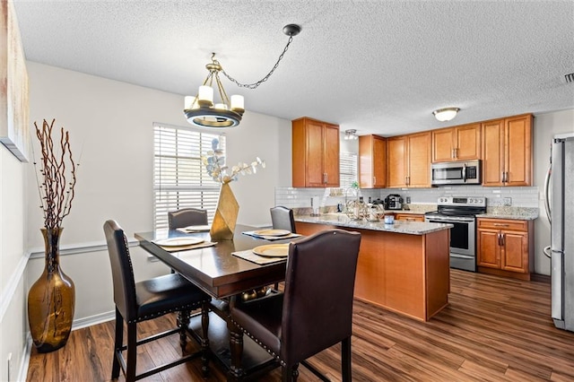 kitchen featuring a textured ceiling, kitchen peninsula, stainless steel appliances, dark wood-type flooring, and an inviting chandelier