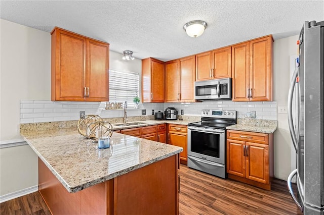 kitchen featuring light stone countertops, sink, kitchen peninsula, stainless steel appliances, and dark wood-type flooring