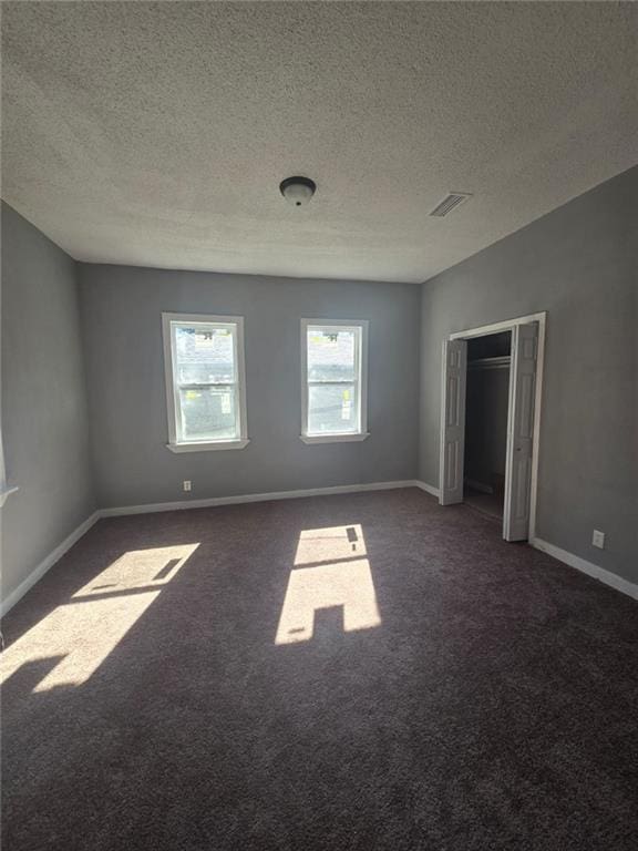 unfurnished room featuring a textured ceiling and dark carpet