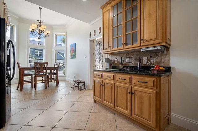 kitchen featuring dark stone countertops, pendant lighting, a notable chandelier, crown molding, and backsplash