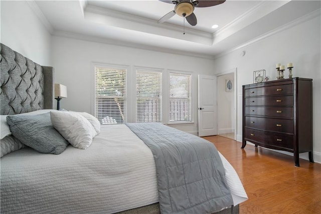 bedroom with a raised ceiling, ceiling fan, ornamental molding, and hardwood / wood-style flooring