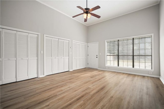 unfurnished bedroom featuring light wood-type flooring, crown molding, ceiling fan, and two closets