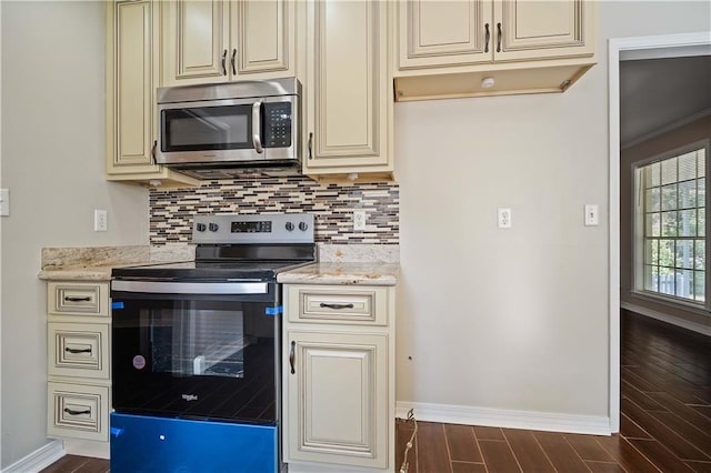 kitchen featuring cream cabinets, tasteful backsplash, dark wood-type flooring, stainless steel appliances, and light stone countertops