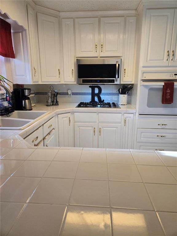 1832 Aden Rd, Mobile, AL 36695 - kitchen with oven, stainless steel microwave, tile counters, gas stovetop, and white cabinetry