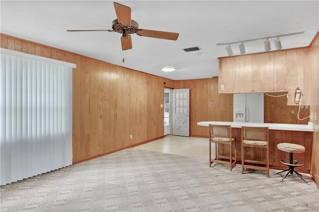 kitchen with ceiling fan, white fridge with ice dispenser, kitchen peninsula, and wooden walls