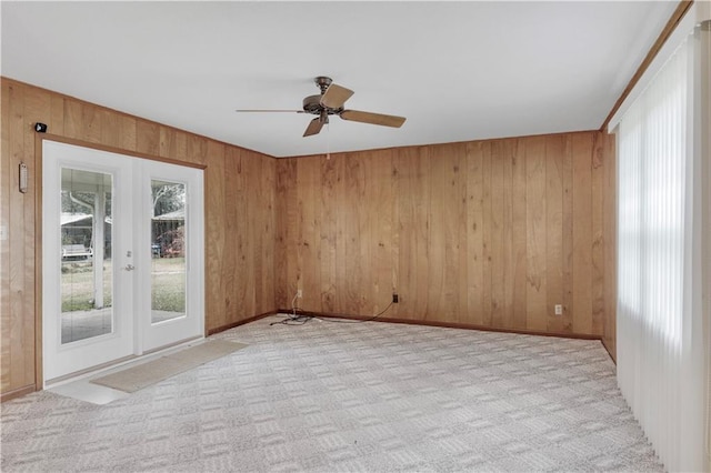 carpeted spare room featuring a wealth of natural light, wooden walls, french doors, and ceiling fan