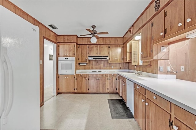 kitchen with ceiling fan, sink, white appliances, and wooden walls