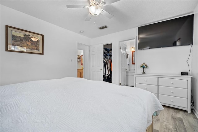 bedroom with ensuite bath, a walk in closet, ceiling fan, and light wood-type flooring