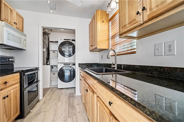 kitchen with sink, light wood-type flooring, double oven range, dark stone counters, and stacked washing maching and dryer